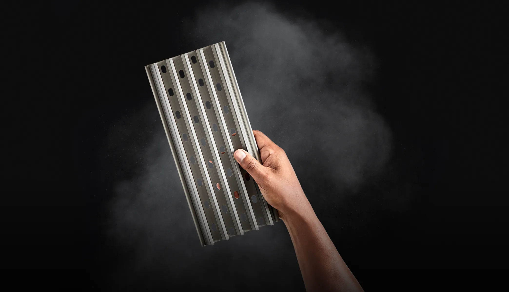 Hand holding a GrillGrate with smoke in the background