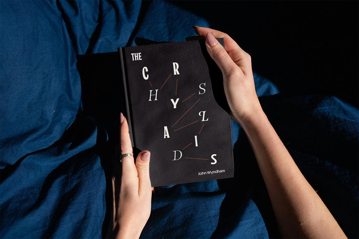 Two hands holding a black book with a title reading "The Chrysalids"