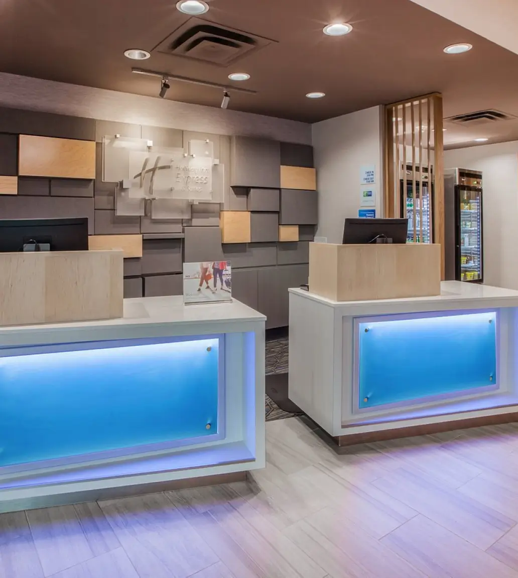 Modern hotel reception area with two white desks featuring blue illuminated panels and a Holiday Inn Express logo on the wall behind.