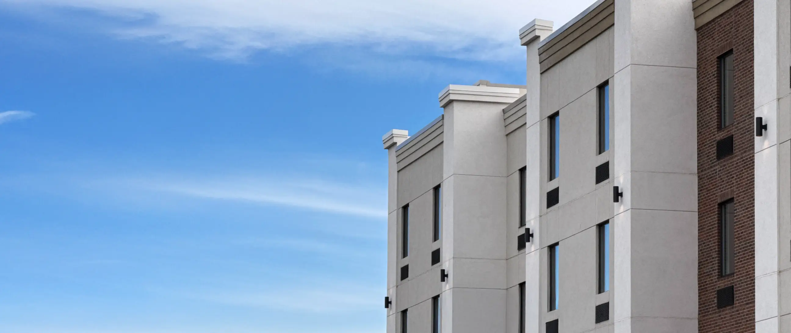 Side view of a modern multi-story building with beige and brick exterior under a clear blue sky.