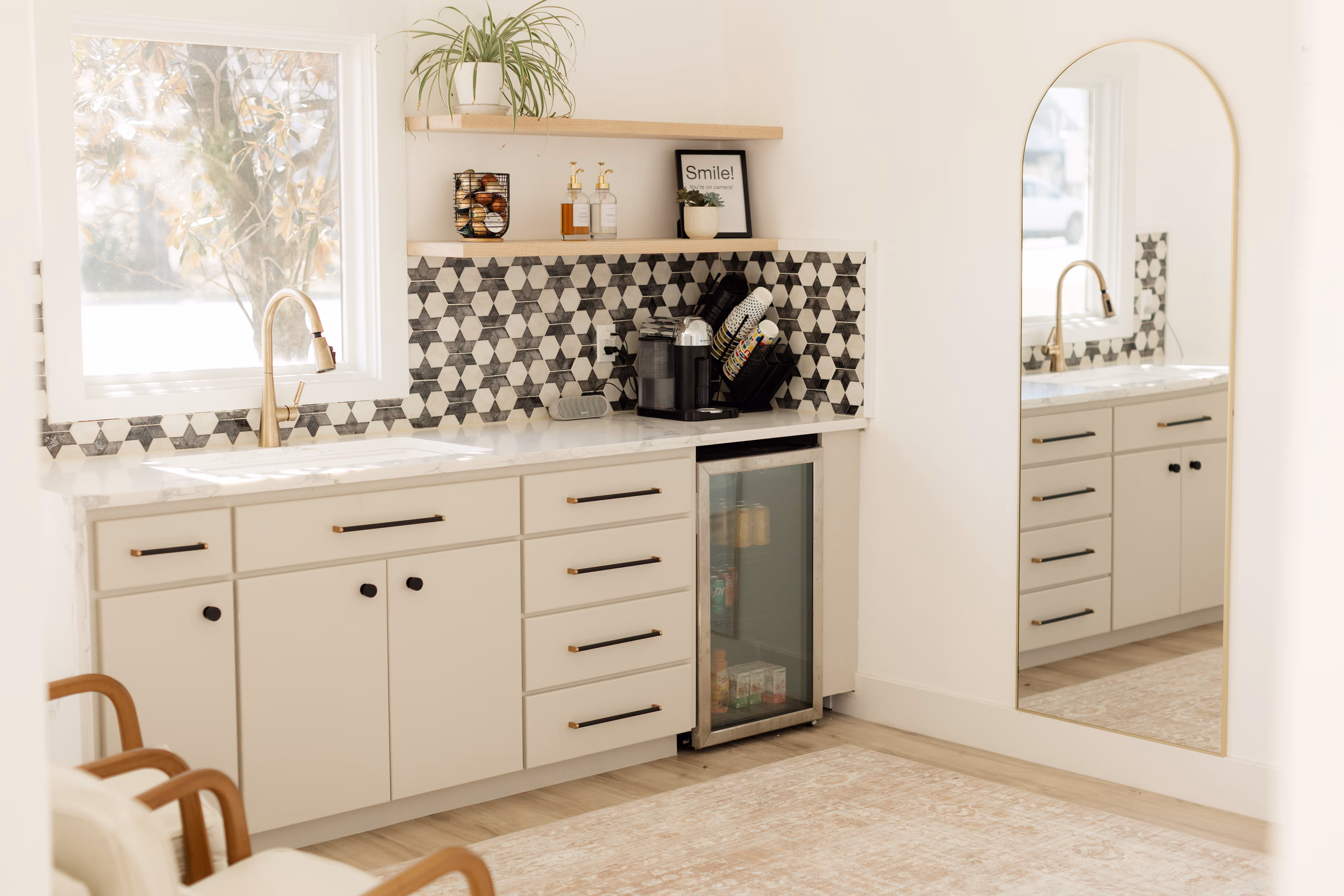 A coffee bar featuring a coffee machine, sink, cups and a mini fridge full of refreshments.