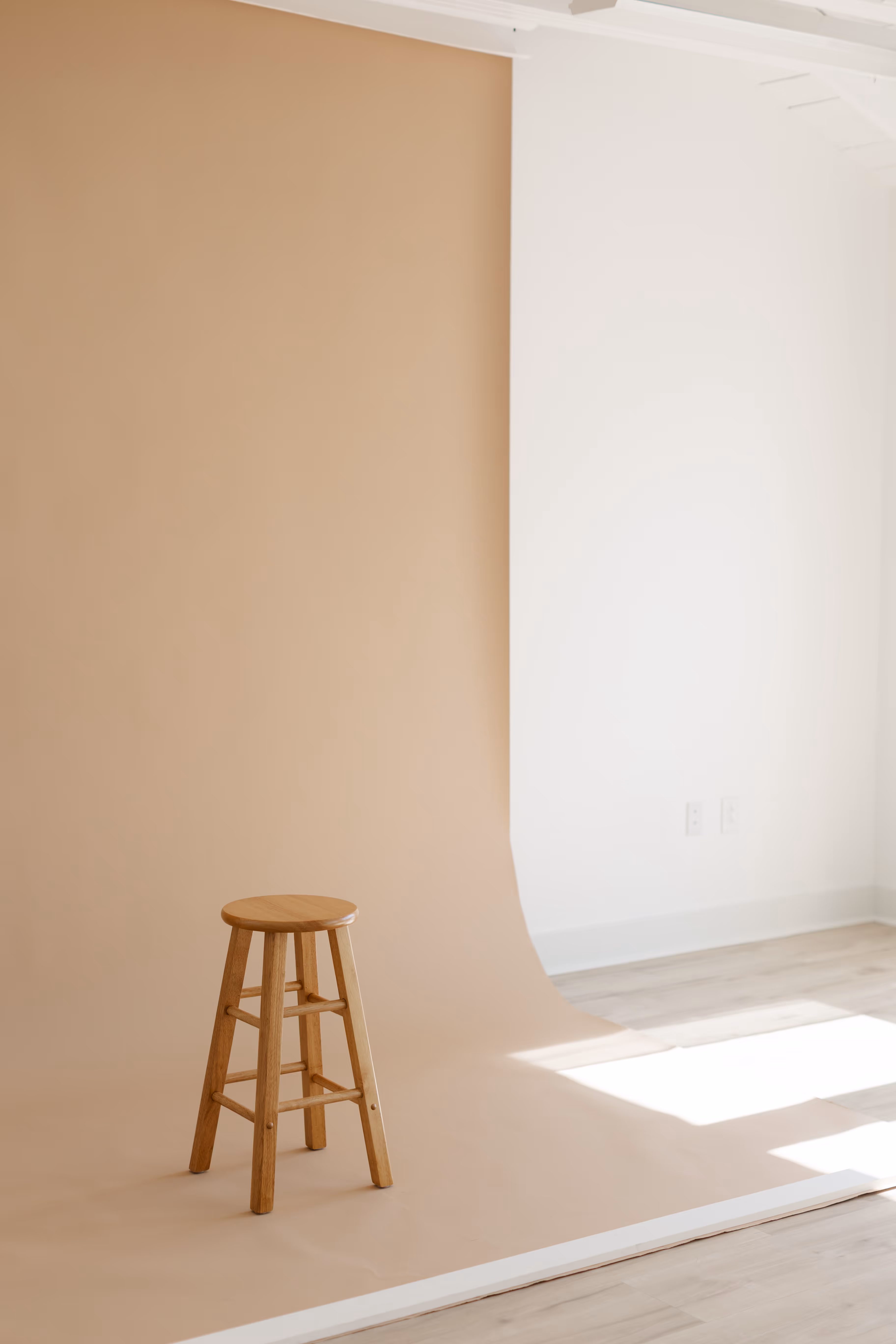A wooden chair sitting in front of a brown backdrop, with natural light coming in through the window.