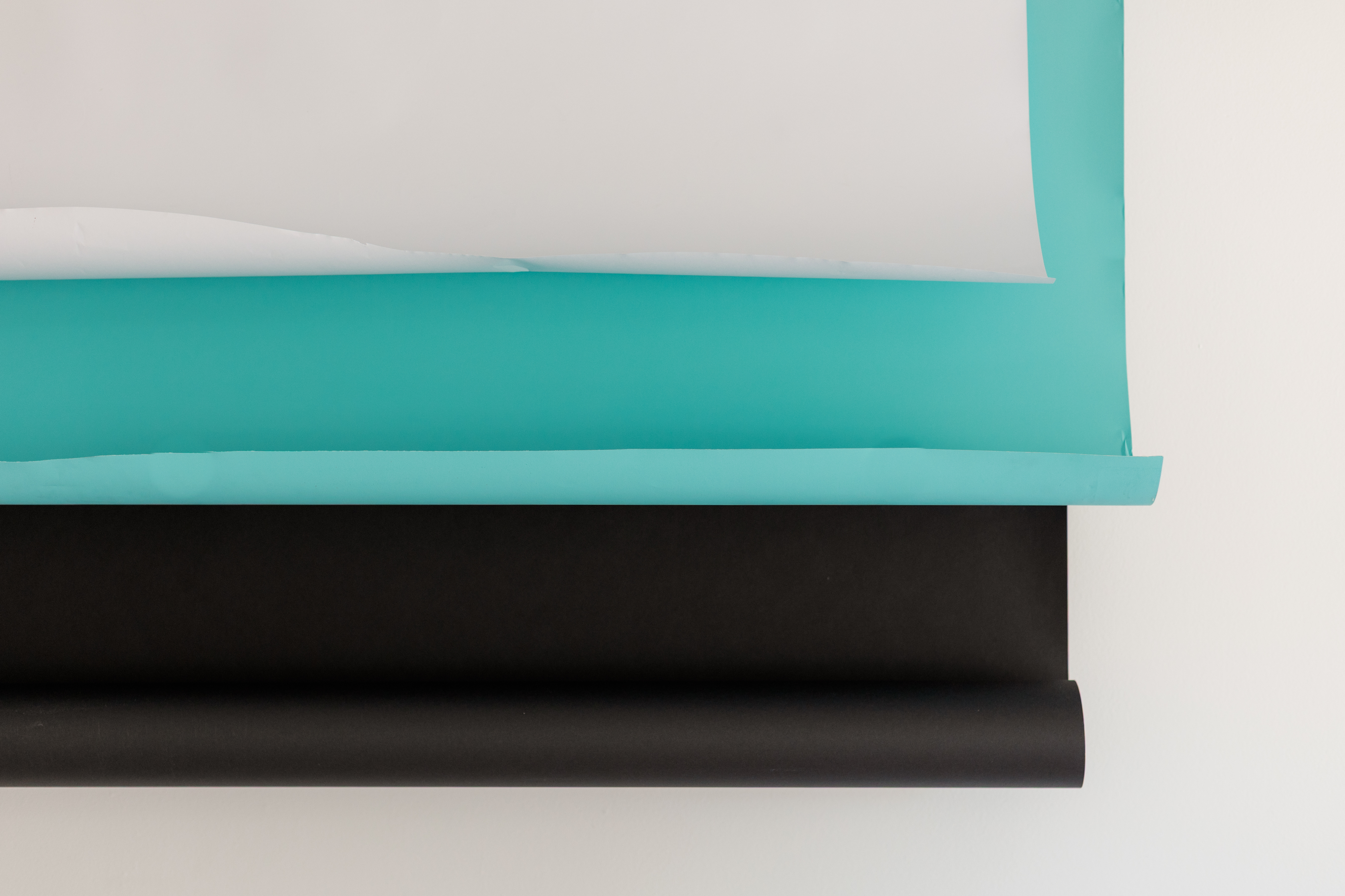 Rolled sheets of paper in white, teal, and black colors stacked horizontally on a white background.