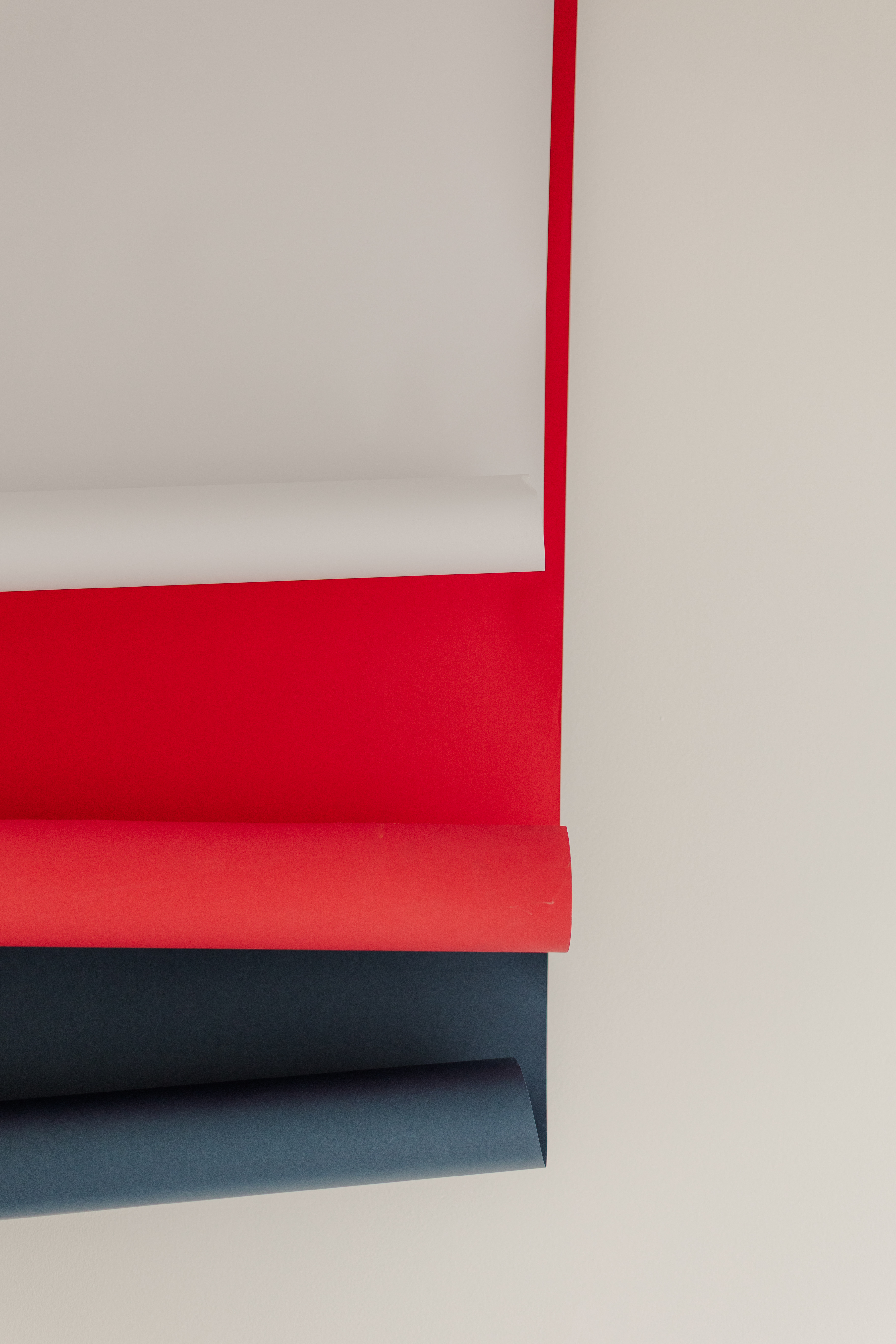 Four rolled sheets of paper in white, red, orange, and dark blue on a light surface.