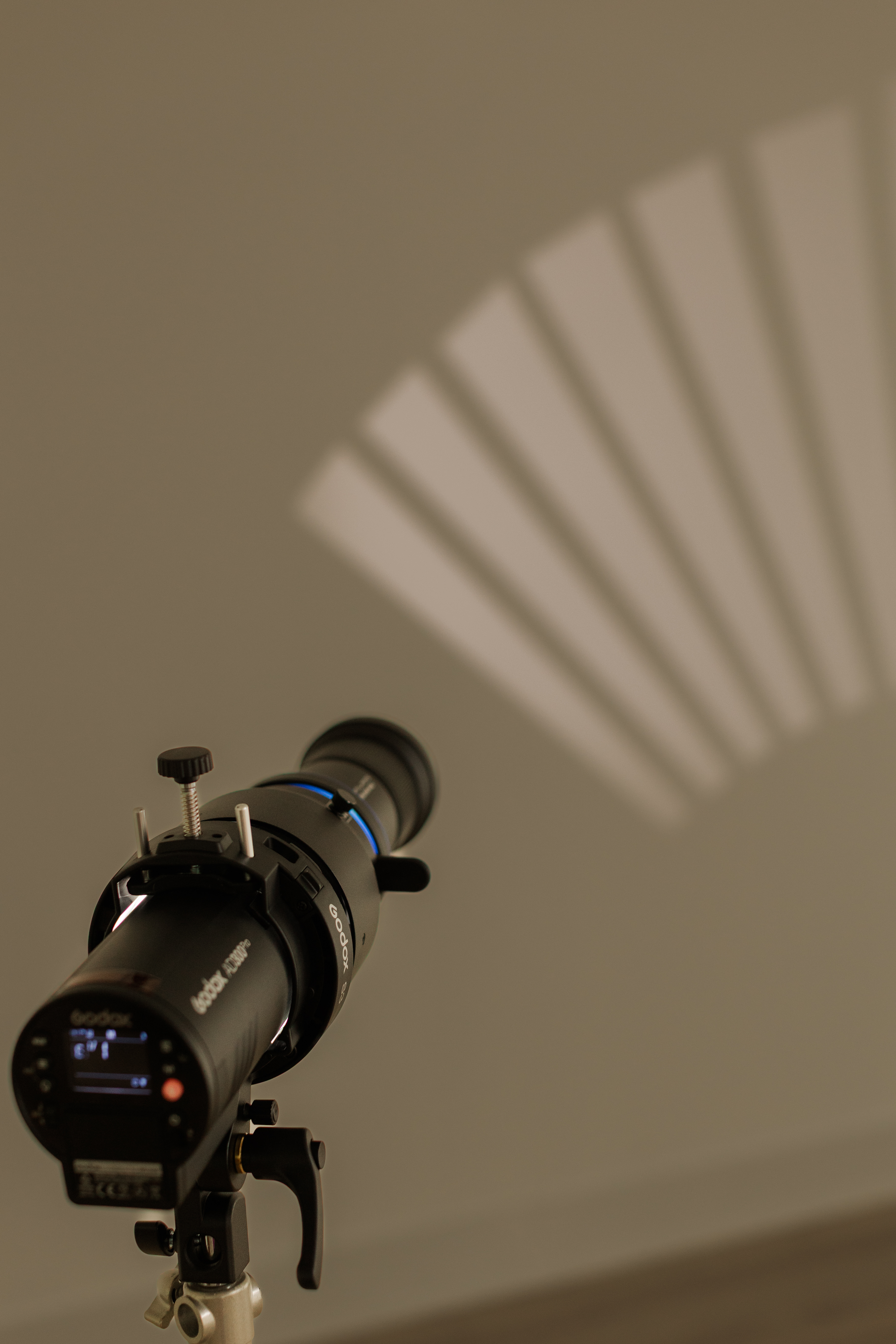Godox camera light projector casting a fan-shaped shadow pattern on a beige wall.