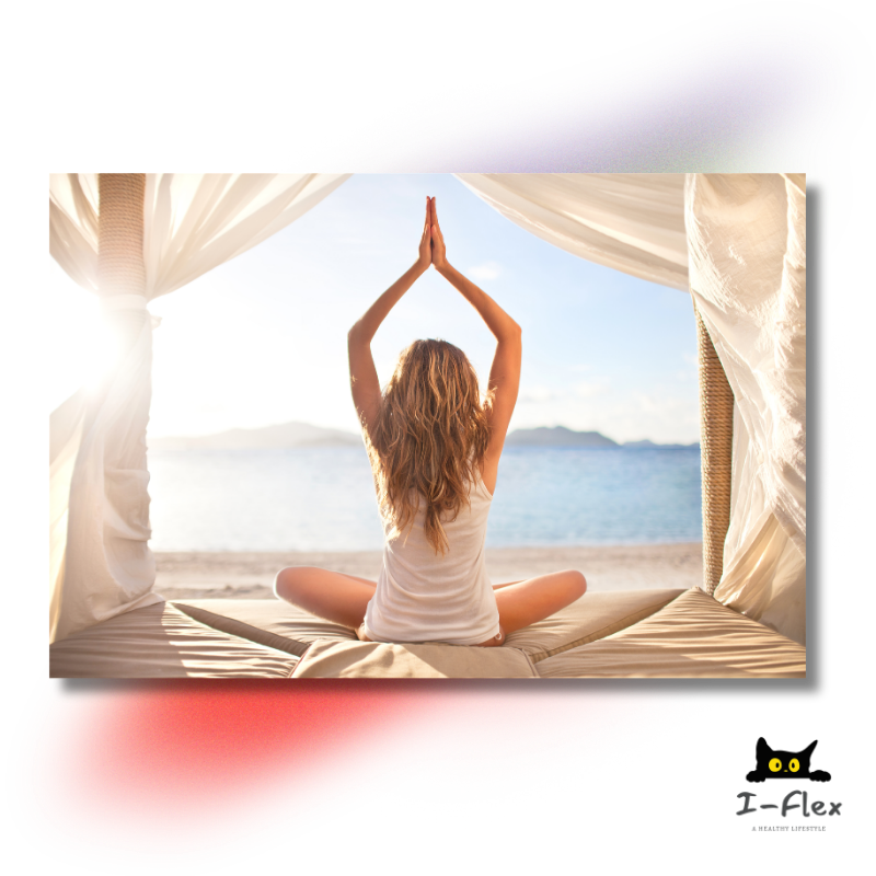 Woman sitting cross-legged in a yoga pose facing the ocean on a sunlit beach under a canopy.