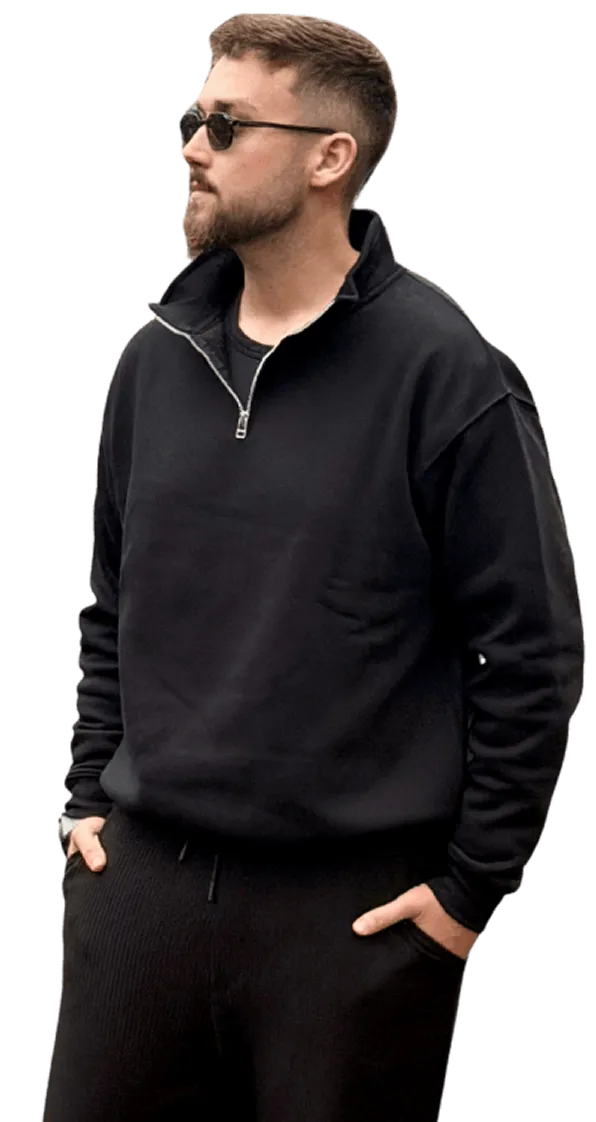 Man with beard and sunglasses wearing a black quarter-zip sweatshirt and black pants with hands in pockets.