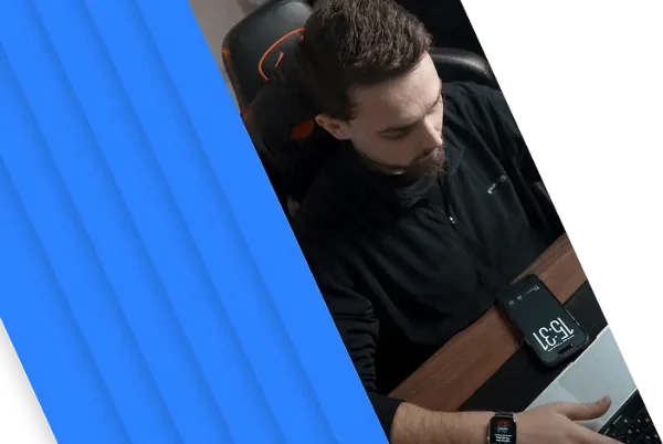 Man with beard working at a desk using a laptop, wearing a smartwatch, with a smartphone showing 15:31 nearby.