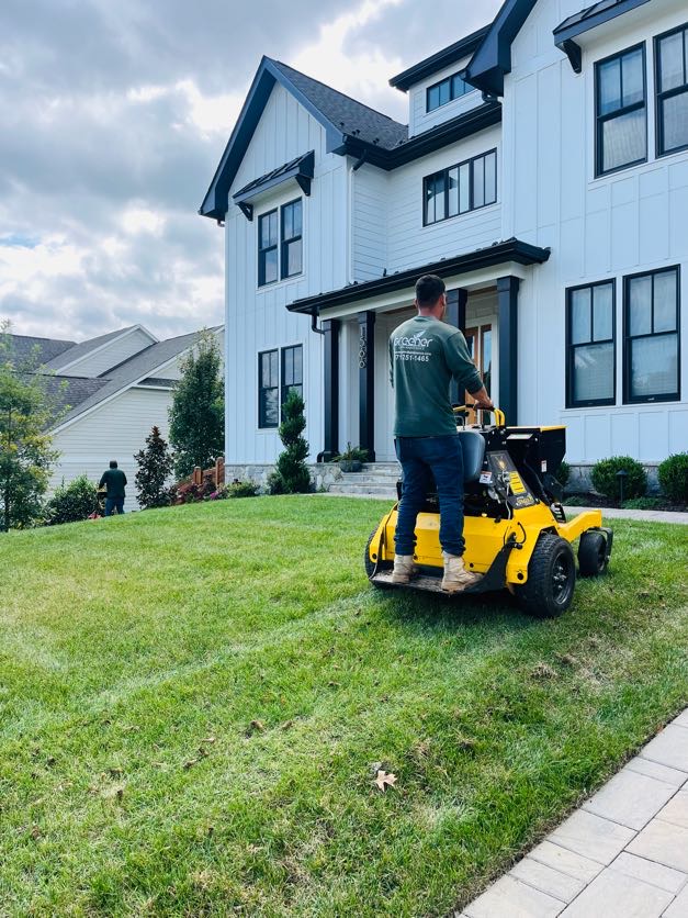 Greener Lawn Maintenance crew member operating a stand-on core aerator across a front lawn at a home in Arlington, VA