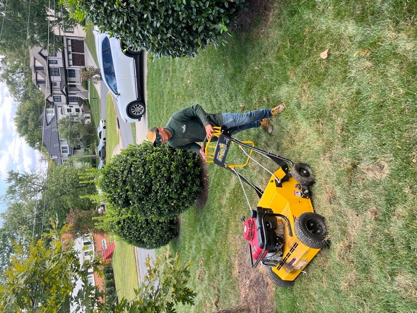 Greener Lawn crew member aerating a residential front yard with a walk-behind aerator in Northern Virginia