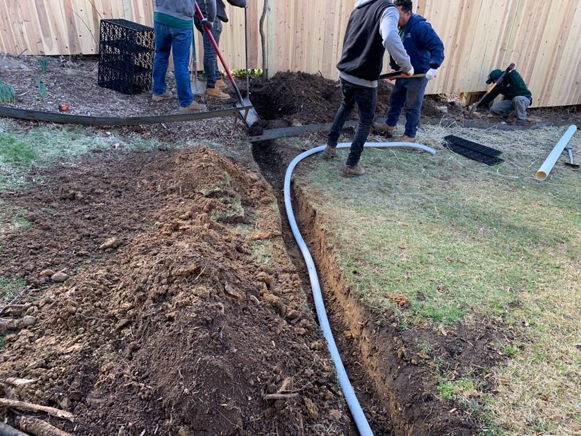 Greener Lawn crew digging a trench and laying drainage pipe in a residential backyard in Arlington, VA