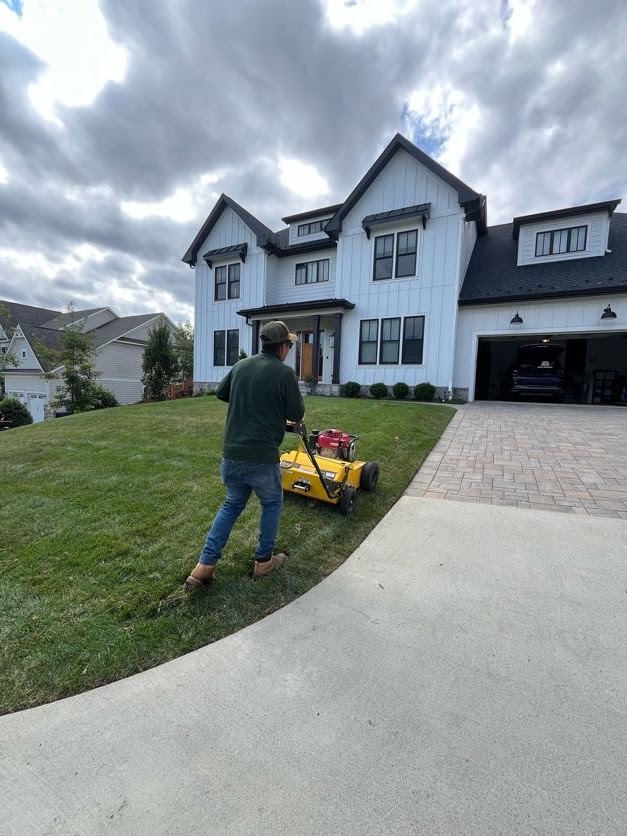 Greener Lawn crew member pushing a motorized top dressing spreader across a front lawn in Arlington, VA