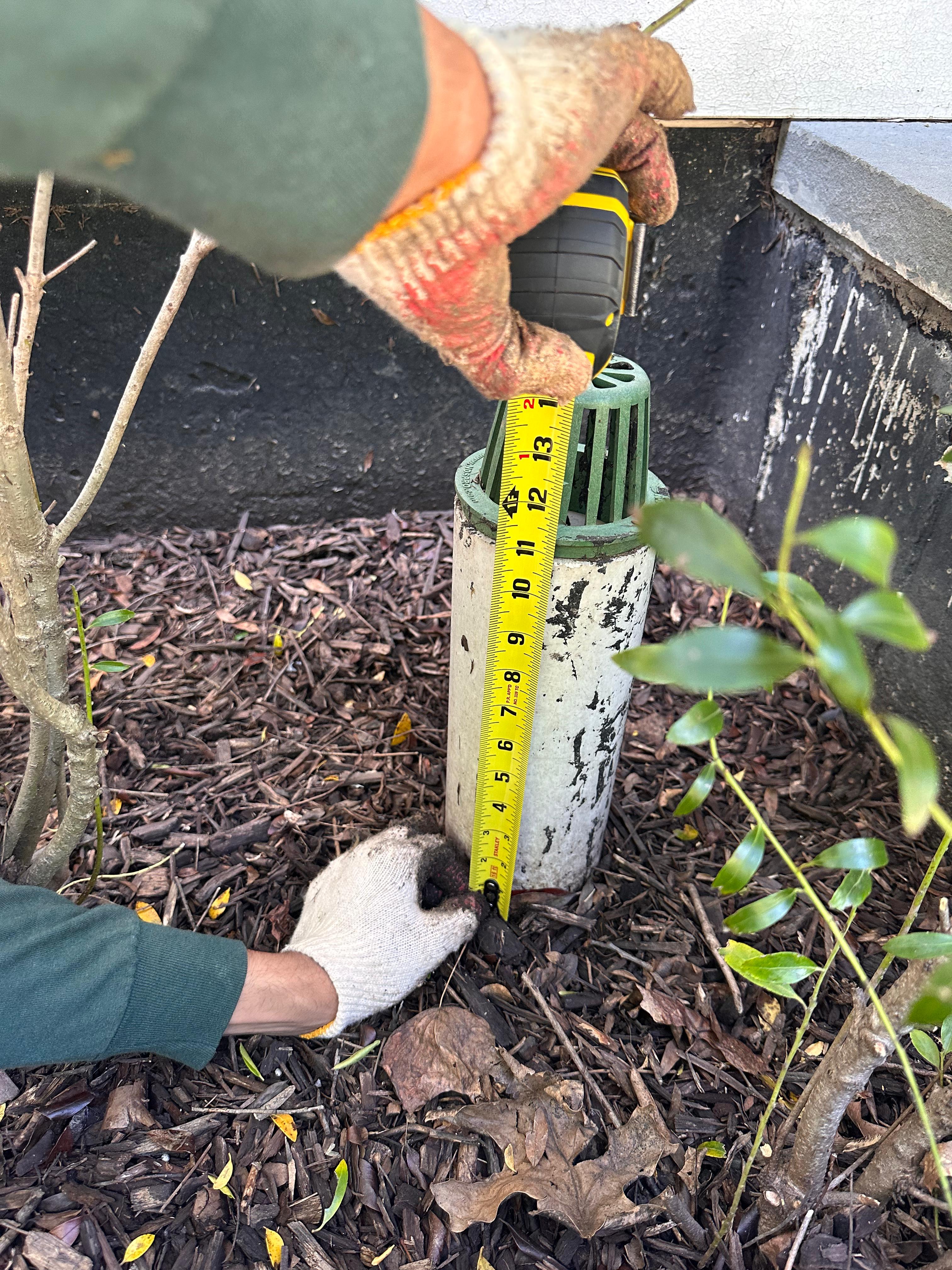 Greener Lawn Maintenance crew member measuring a popup drain emitter in a mulched stormwater bed at a Northern Virginia home