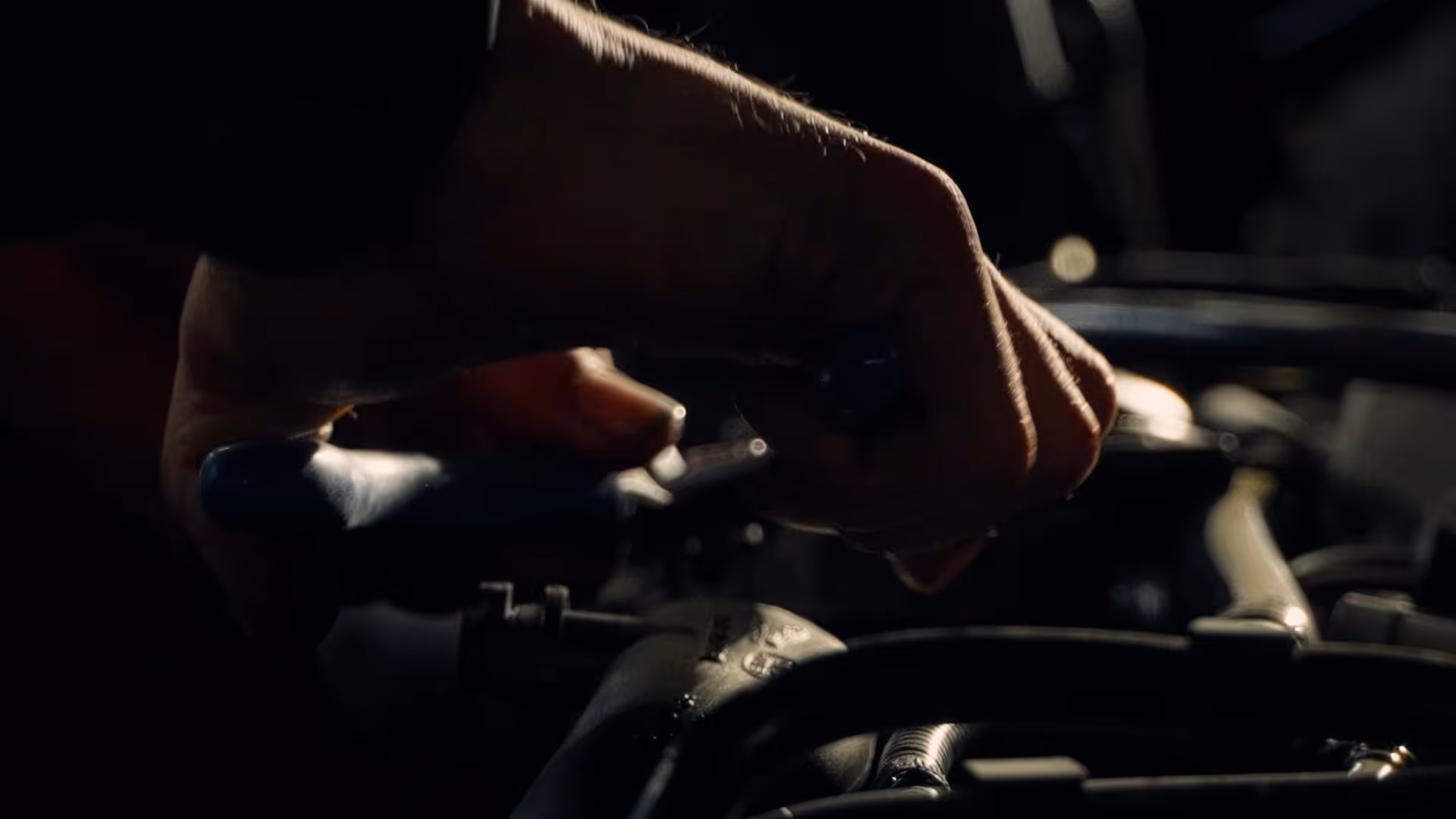 Close-up of a hand using a tool to tighten an oil filter in a car engine.