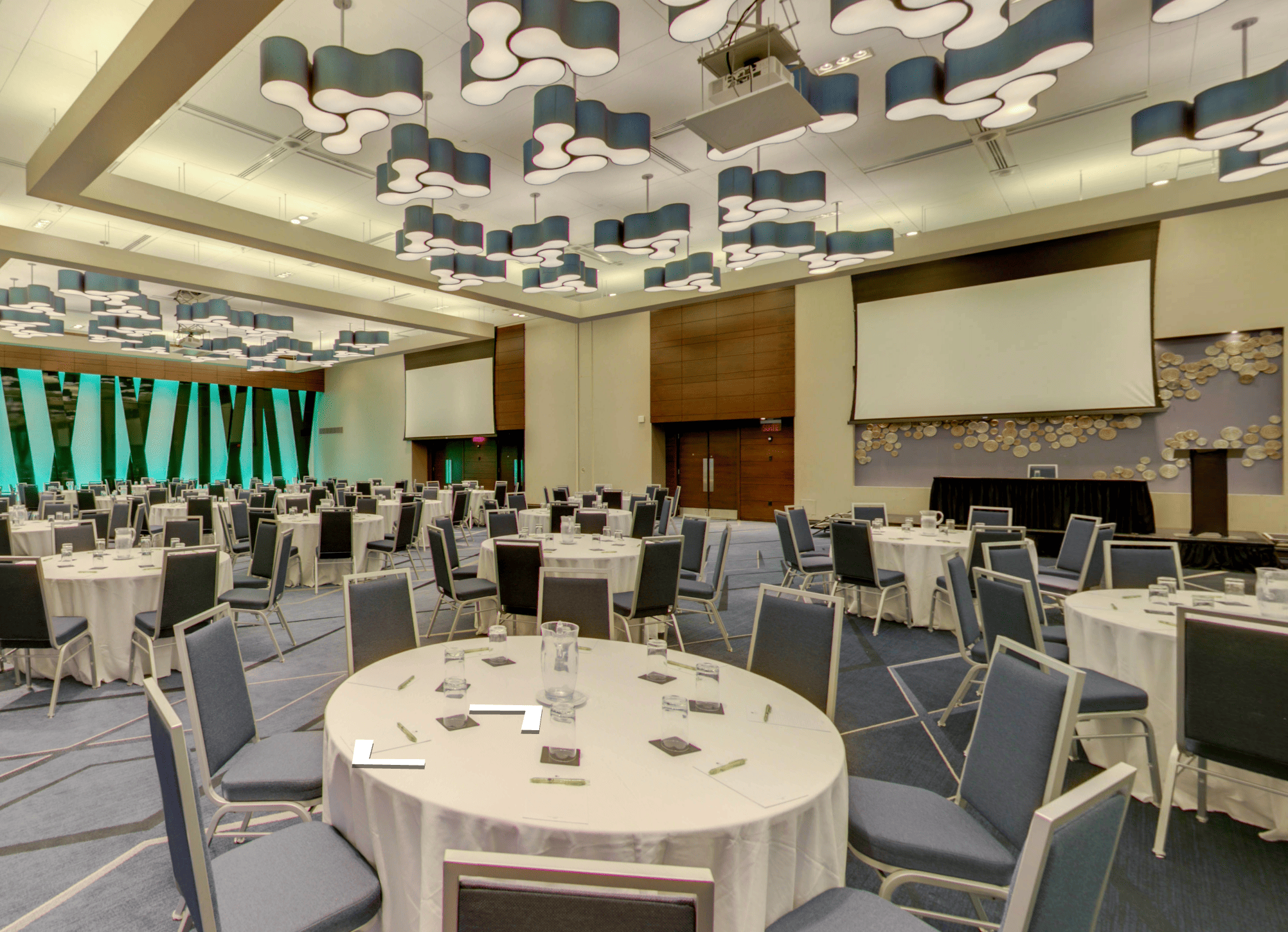 Large conference room set up with round tables covered in white tablecloths and blue chairs under modern ceiling lights.
