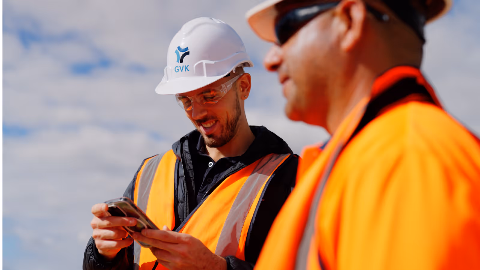 Construction workers in safety gear reviewing information on a smartphone at a job site