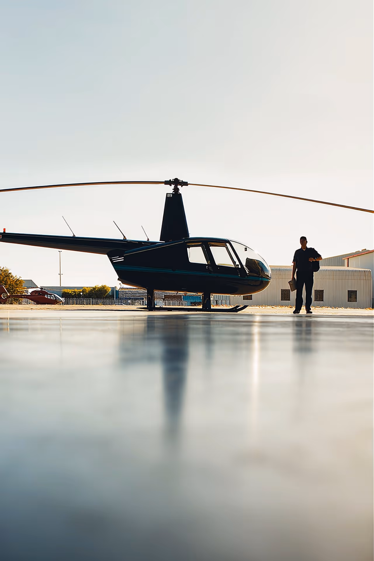 Hélicoptère noir stationné au sol avec une personne debout à côté dans un hangar d'aéroport.