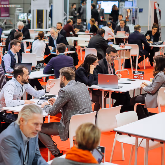 Personnes en tenue professionnelle discutant et utilisant des ordinateurs portables lors d'un événement de réseautage avec des tables blanches et un sol rouge.