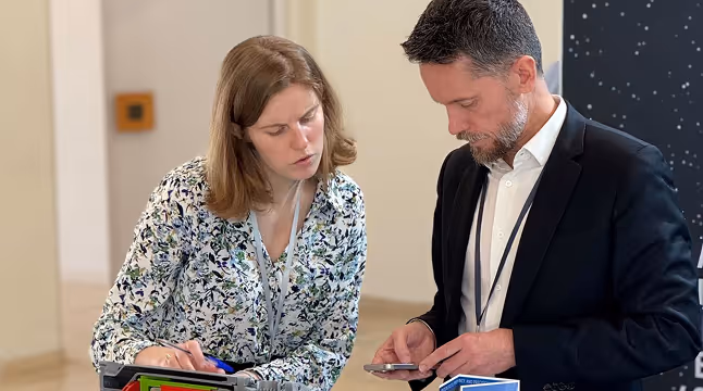 Deux professionnels discutent, la femme consulte un appareil et l'homme regarde son téléphone.
