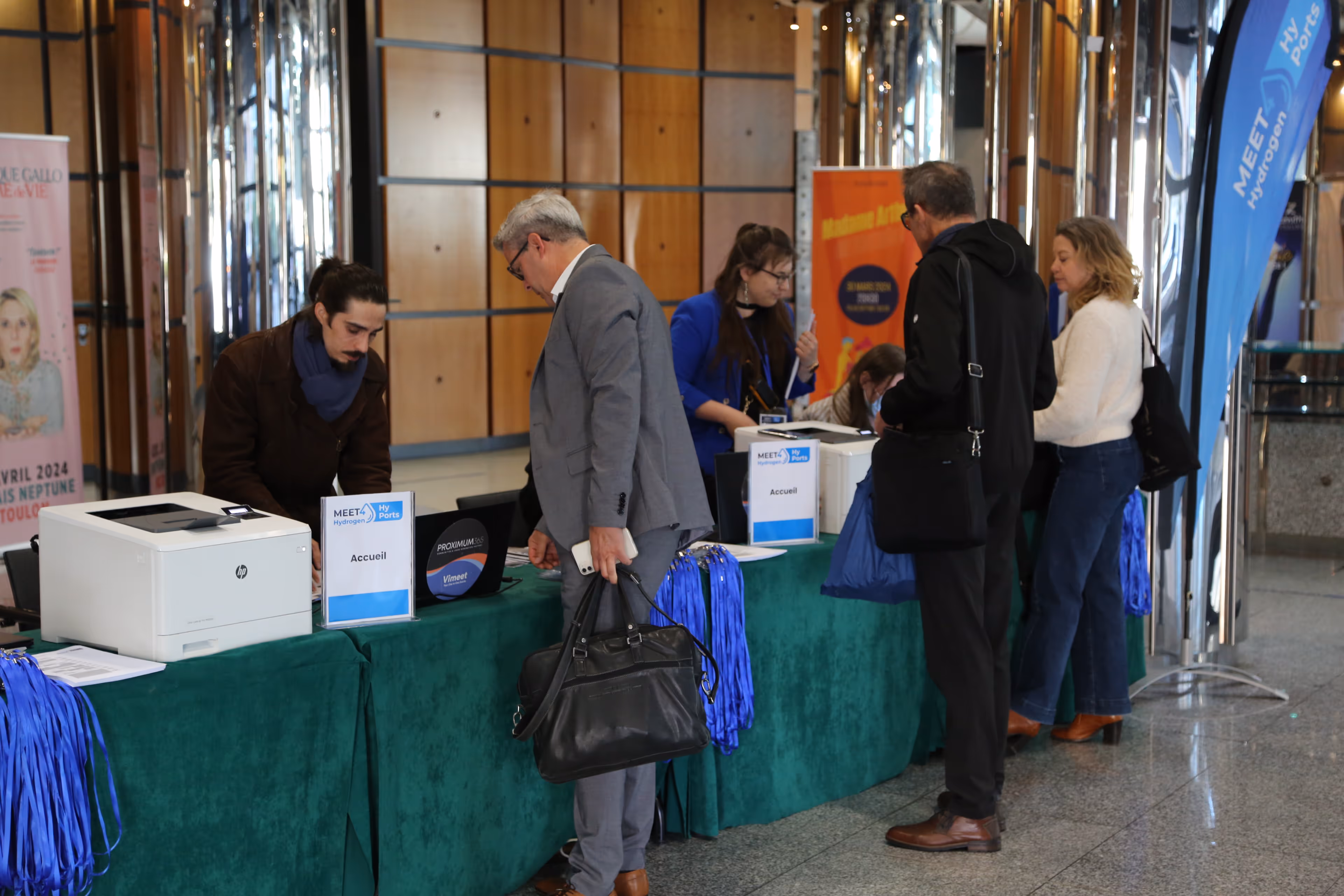Des personnes s'enregistrant à un comptoir d'accueil lors d'un événement avec des bannières MEET Hydrogen HyPorts.