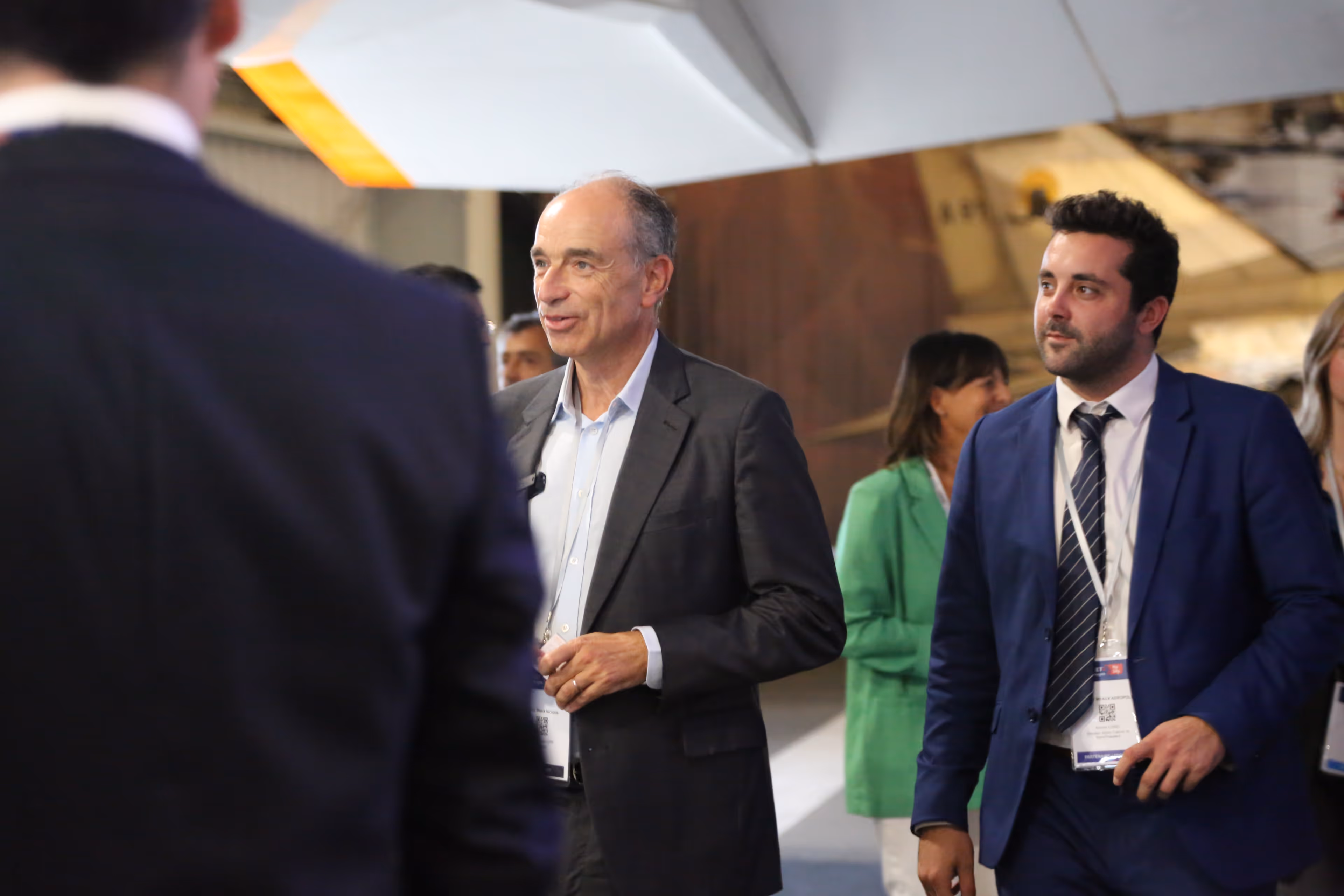 Deux hommes en costume discutant lors d'un événement professionnel en intérieur.