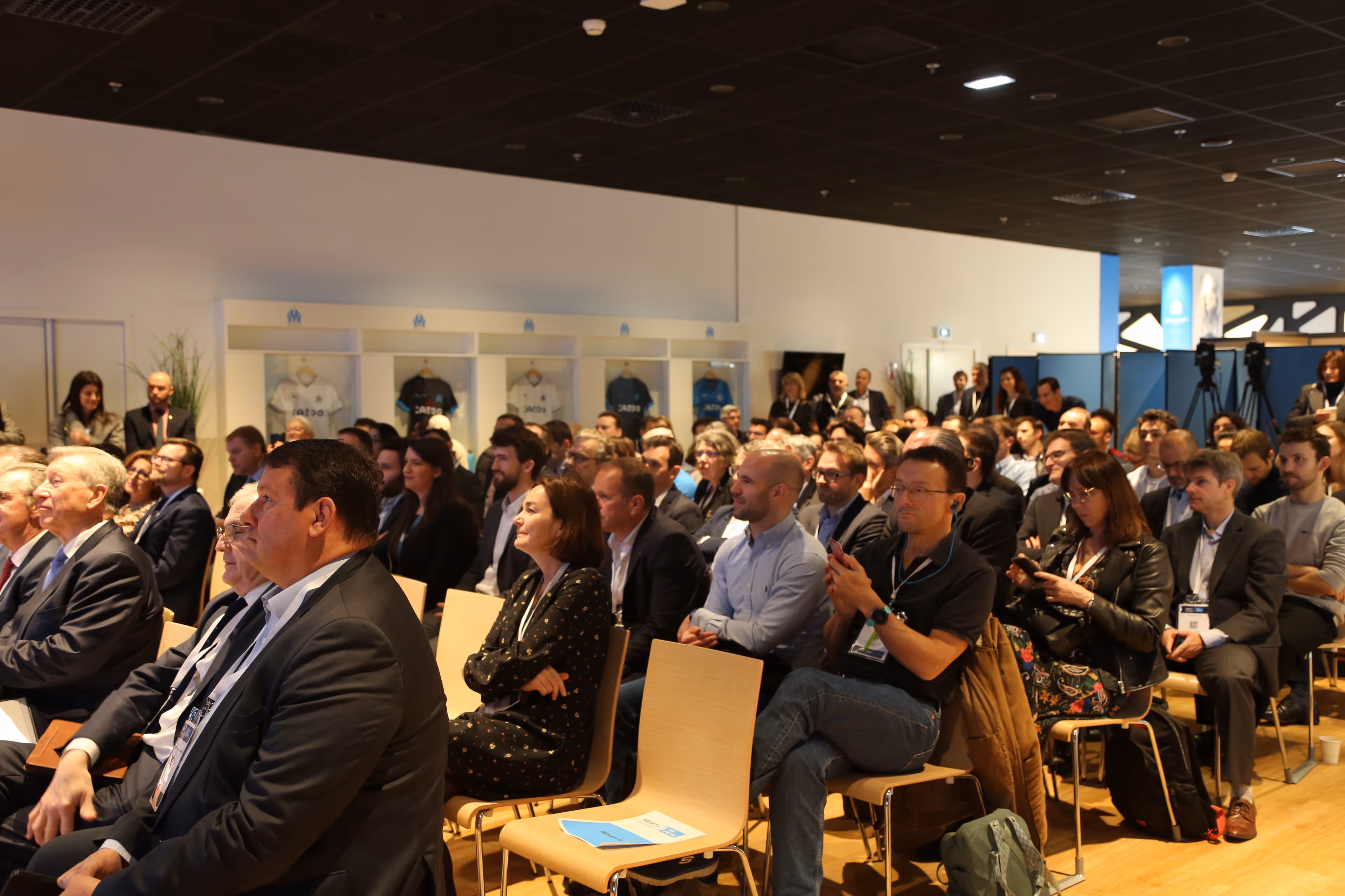 Un groupe de personnes assises dans une salle de conférence, écoutant une présentation.