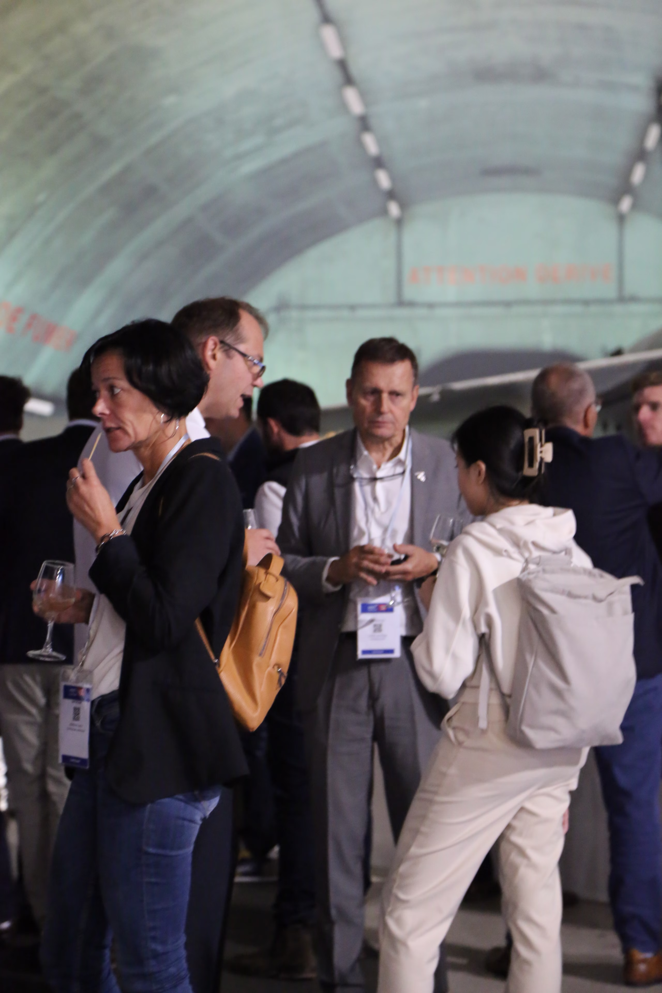 Un groupe de personnes discutant dans une salle voûtée lors d'un événement professionnel, certaines tenant des verres à vin.