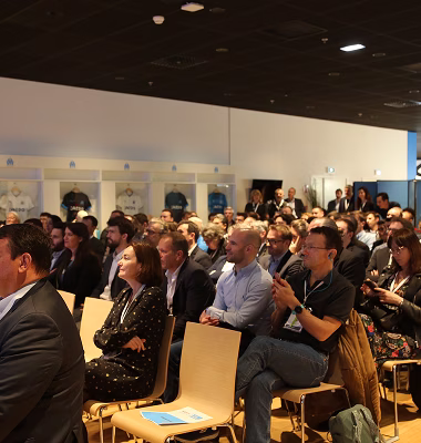 Un groupe de personnes assises dans une salle, attentives à une présentation ou conférence.