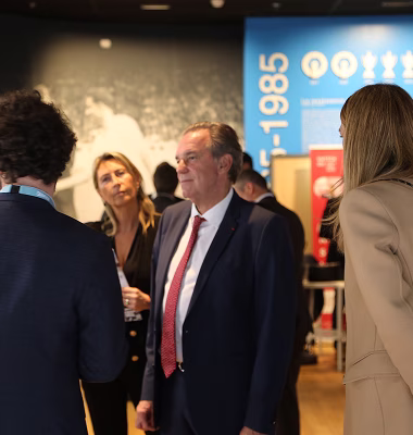 Quatre adultes en conversation dans un espace intérieur, deux hommes en costume et deux femmes dont une de dos.