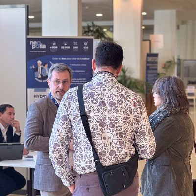 Trois personnes discutant lors d'un événement professionnel dans un espace intérieur clair.