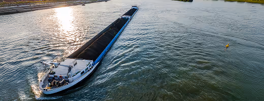 Grand bateau cargo naviguant sur une large rivière au coucher du soleil.