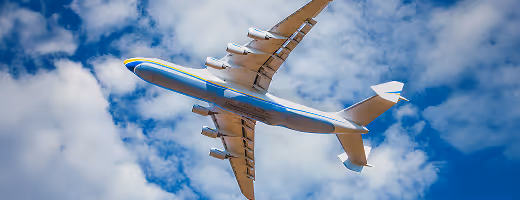 Avion de ligne volant dans un ciel bleu partiellement nuageux vu de dessous.