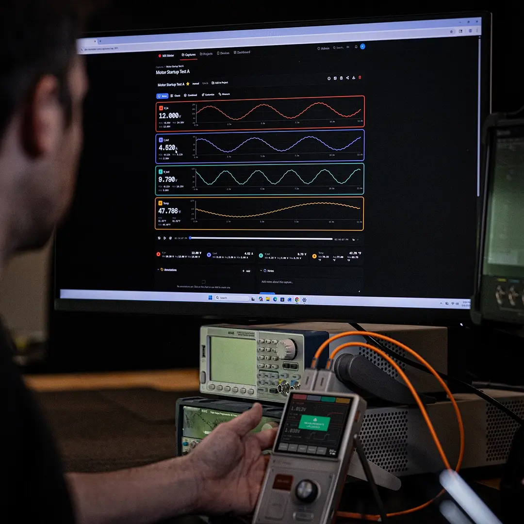 A man with a beard working on internal wiring of an electronic device or computer in a dimly lit room.