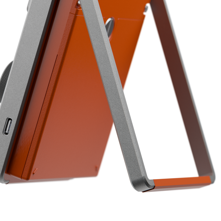 Close-up of an orange electronic device supported by a silver metal kickstand with a USB-C port.