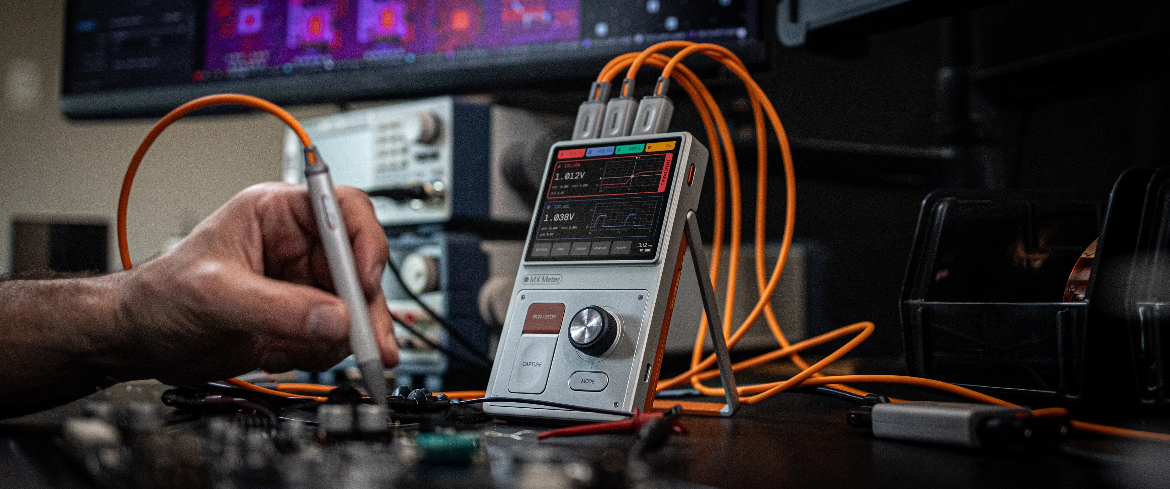 Hand using a probe connected to a digital multimeter displaying voltage and current waveforms.