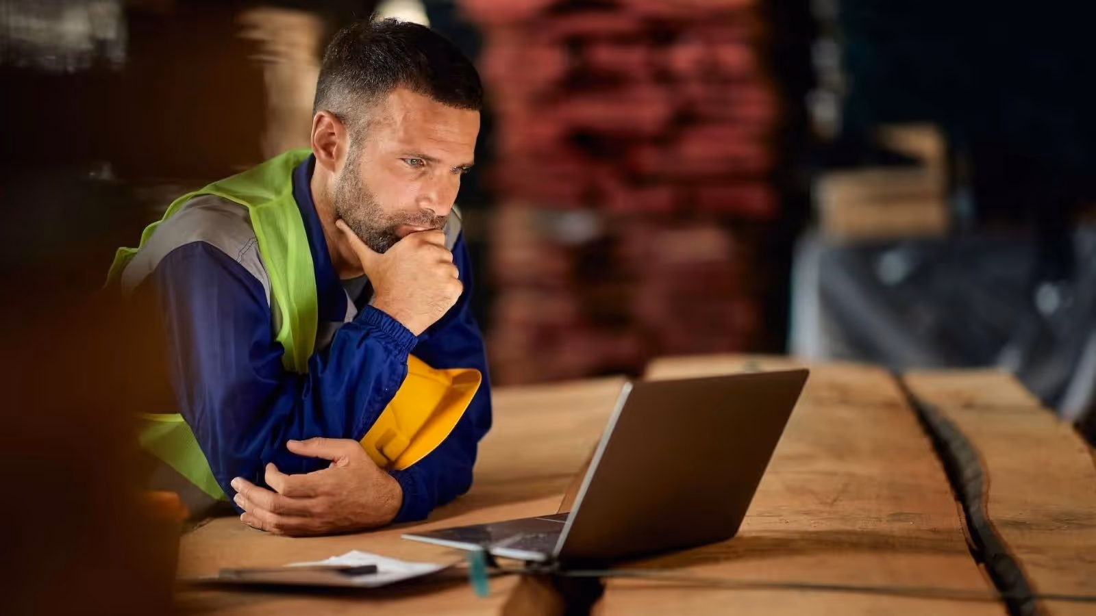 subcontractor looking at his laptop screen, leaning on a wooden surface with blurry background