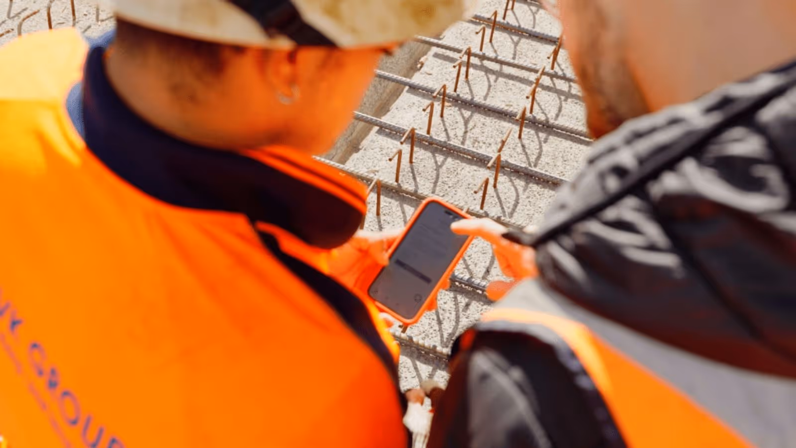 Two subcontractors at a construction site, looking at a phone that has the Neo app opened