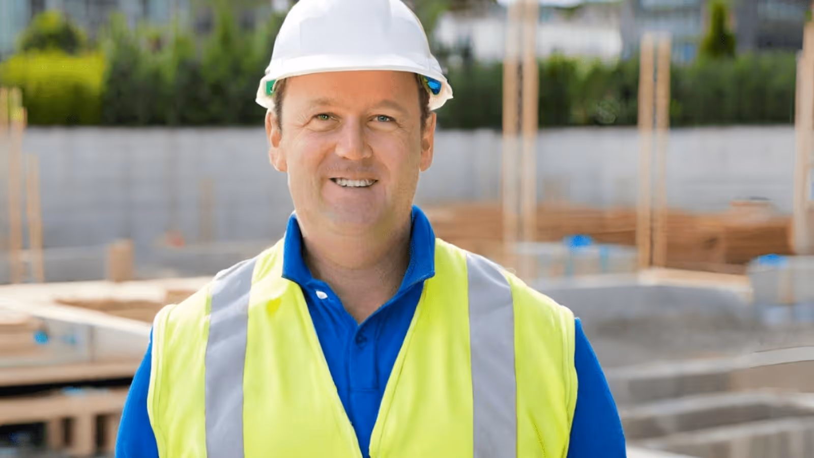 MIddle-aged general manager at a construction site where steel fixing work is executed, smiling into the camera