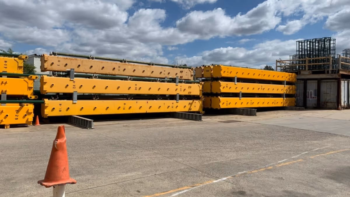 Large yellow steel beams stacked and stored near a large-scale construction site and a bright orange traffic cone placed nearby