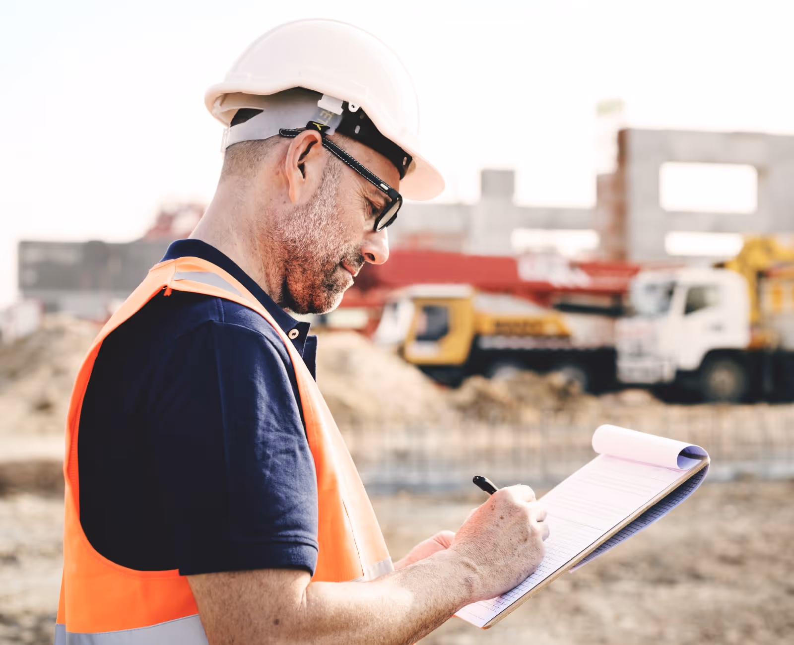 Construction supervisor in safety vest writing notes on a clipboard at a job site