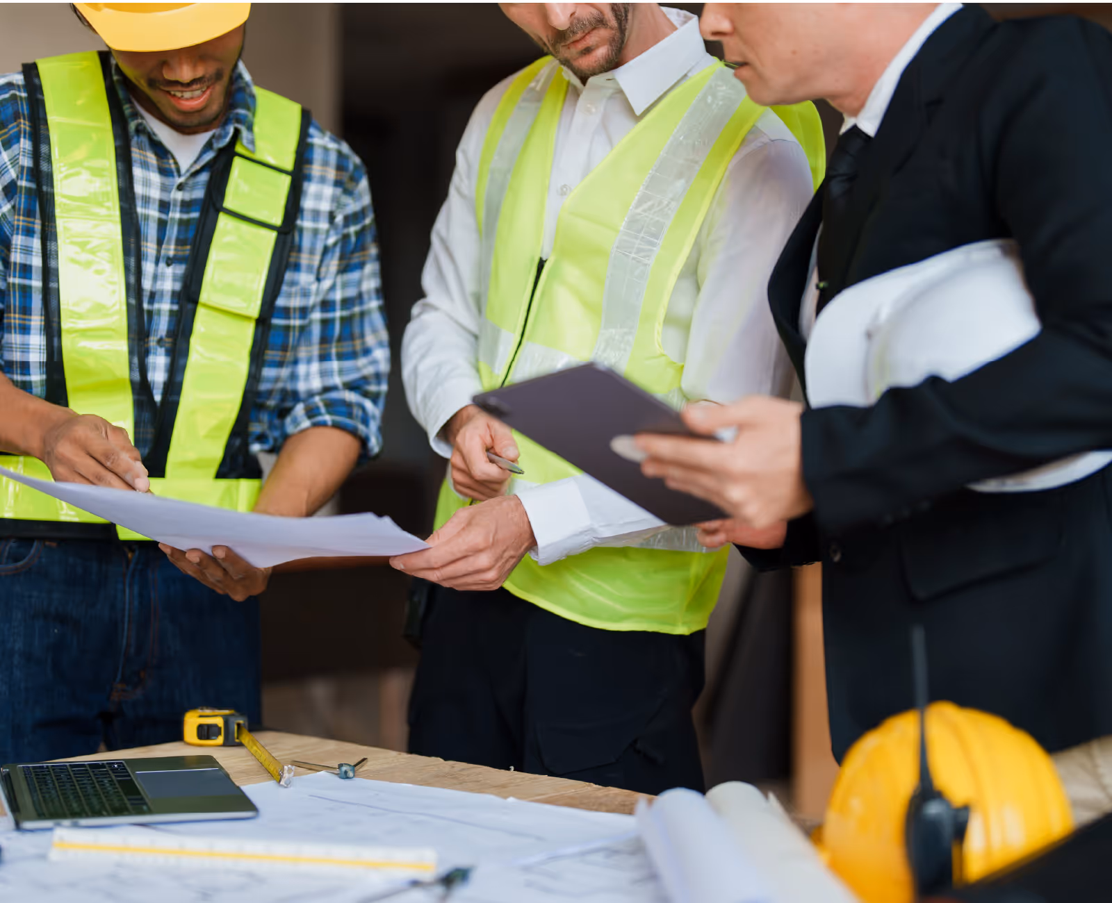 Construction team in safety vests reviewing building plans and documents together
