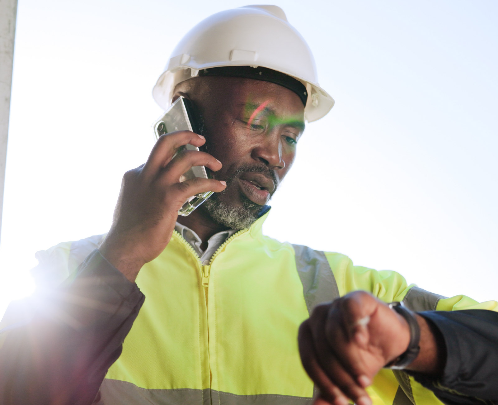 Construction supervisor speaking on a mobile phone while checking the time on a job site