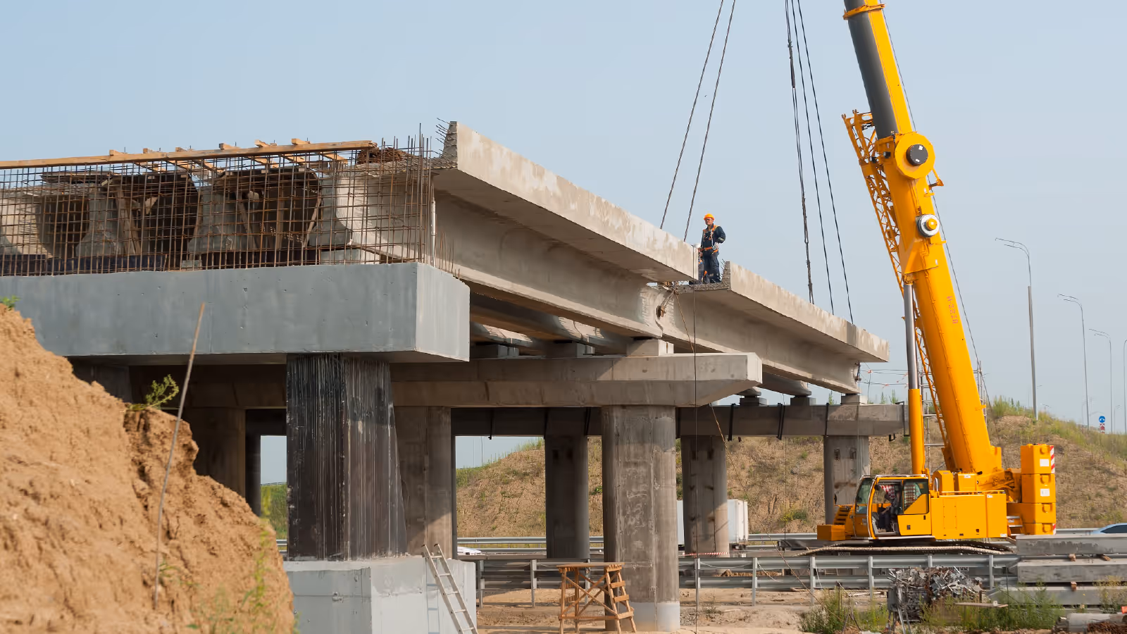 Construction of a concrete bridge with crane lifting materials and workers on site