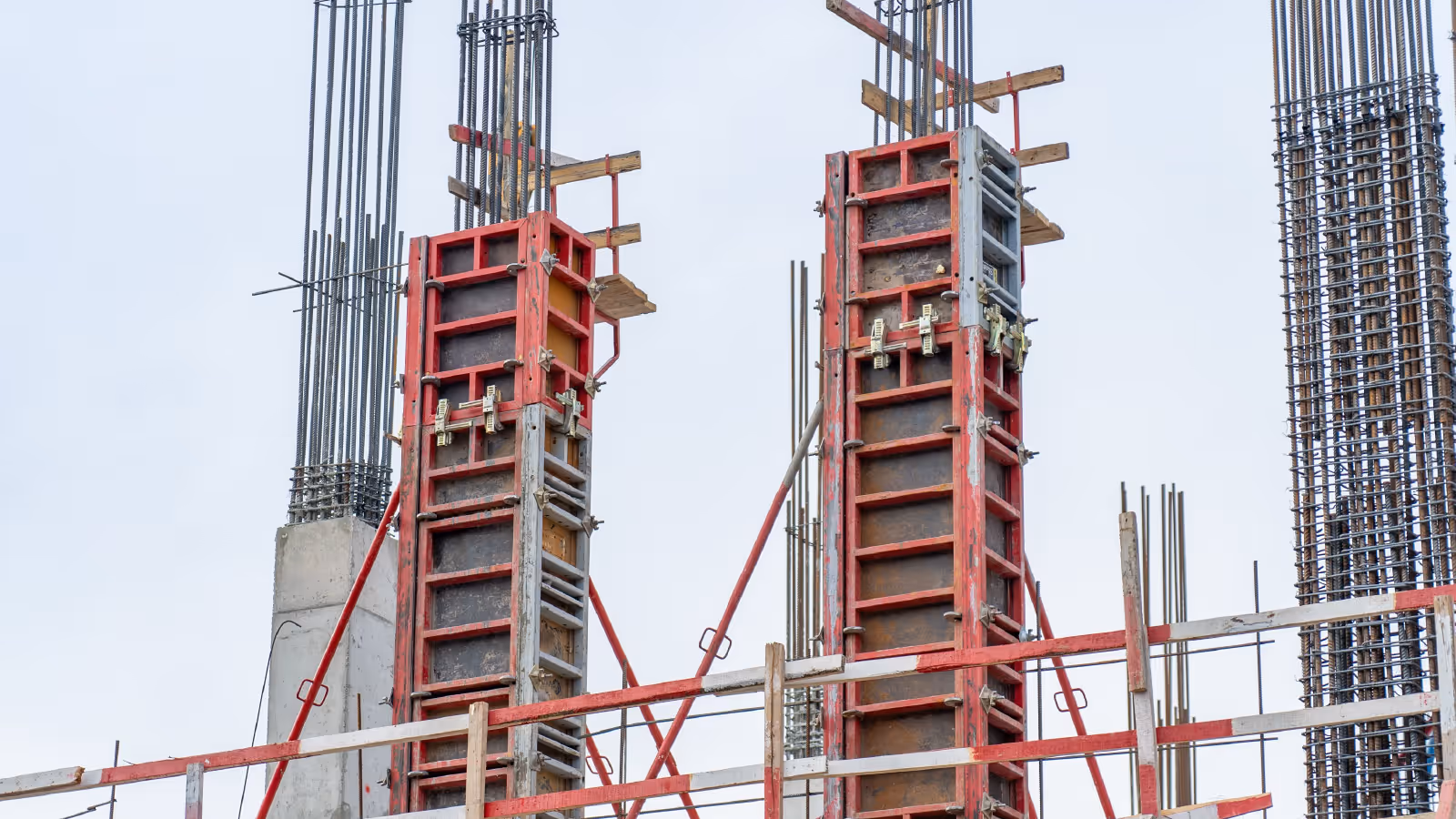 Concrete columns with red formwork systems and exposed steel reinforcement on construction site