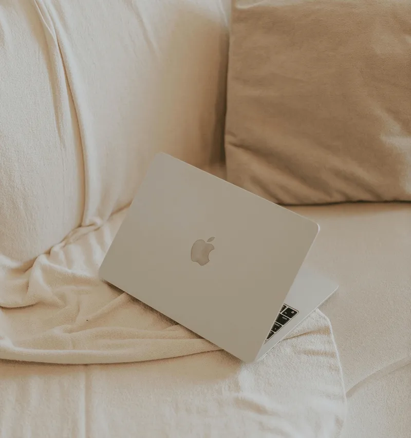 A laptop resting on a cream couch with soft beige pillows