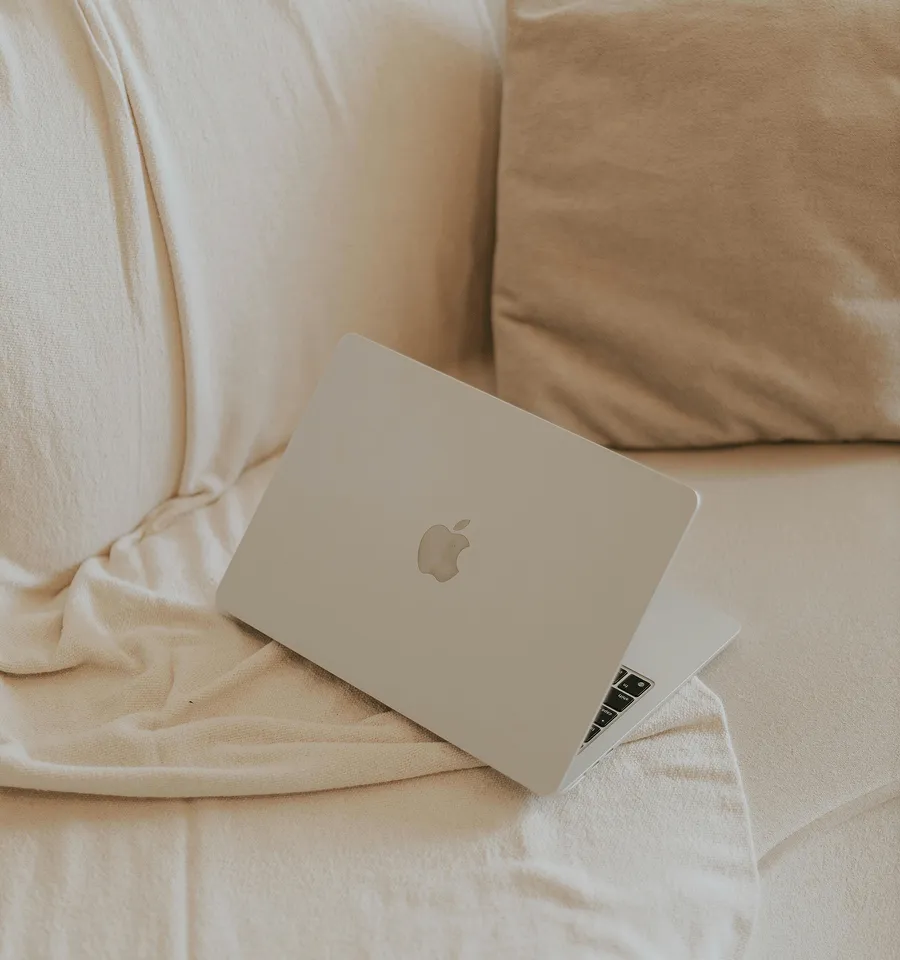 A laptop resting on a cream couch with soft beige pillows