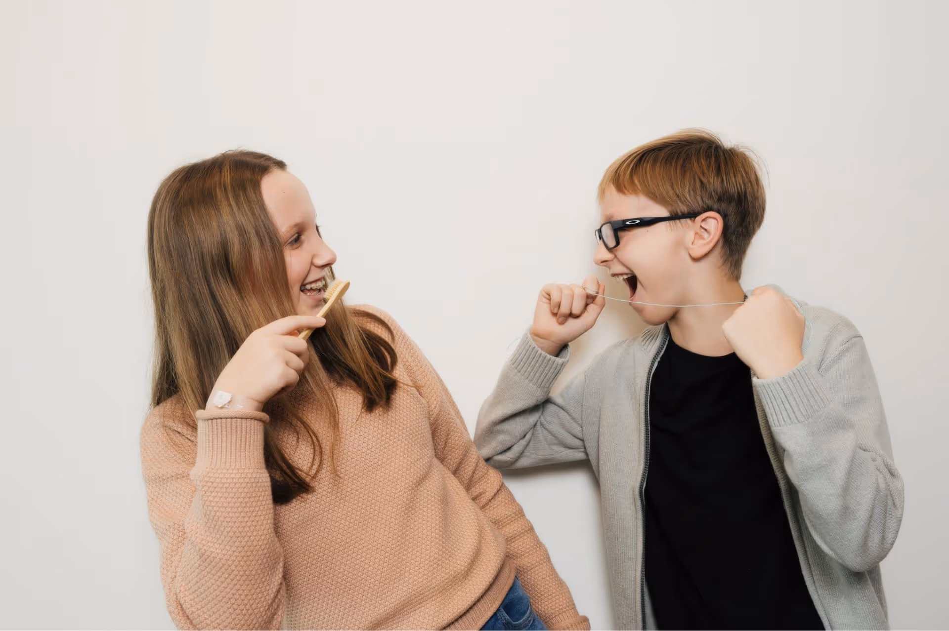Young woman wearing a white sweater is holding a clear dental aligner near her mouth.