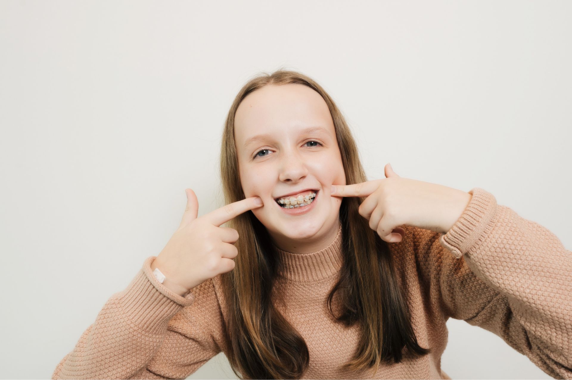 Smiling boy with braces sitting in a dental chair giving a thumbs up, with dental professionals wearing masks in the background.