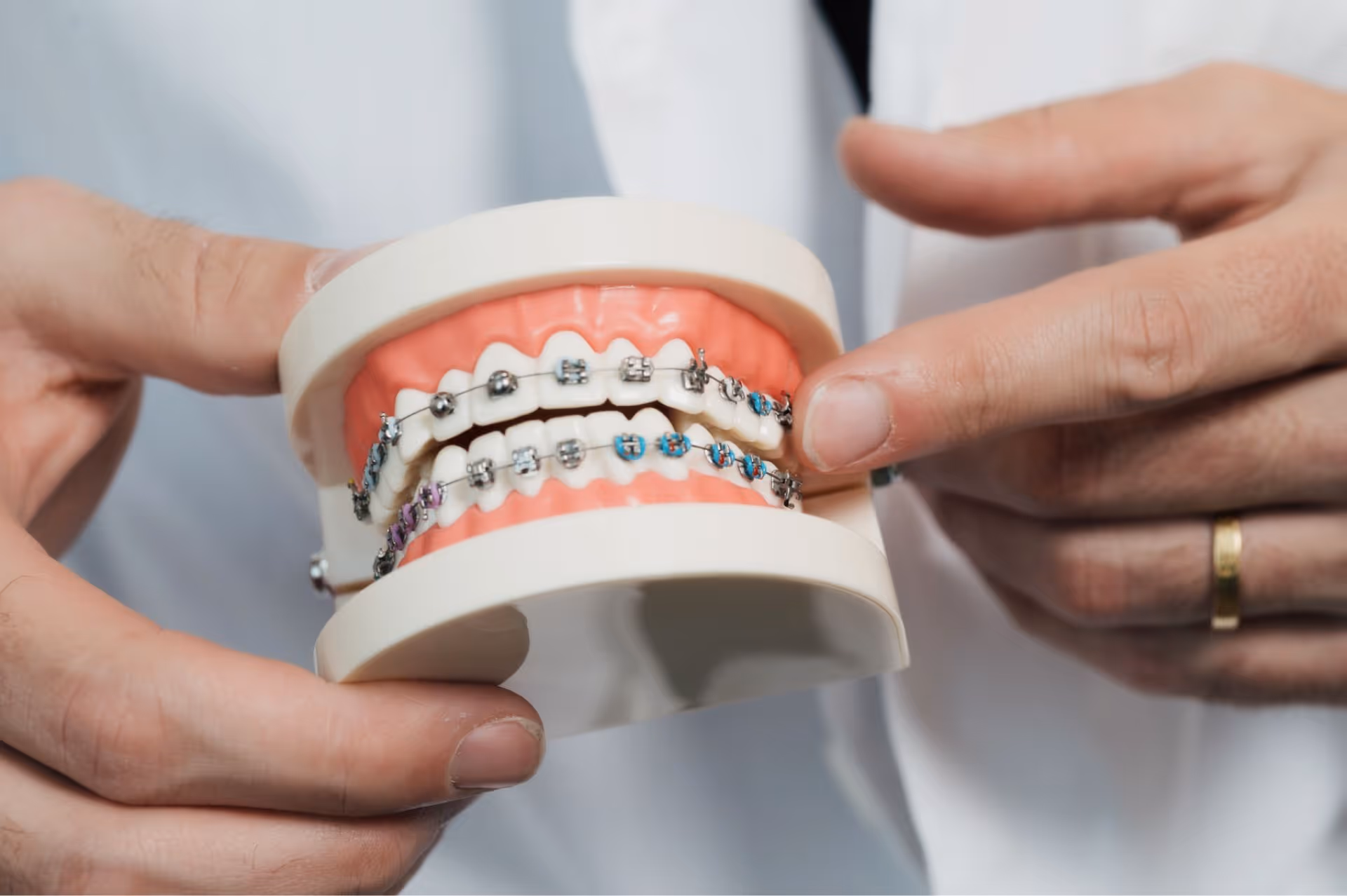 Smiling boy with braces sitting in a dental chair giving a thumbs up, with dental professionals wearing masks in the background.