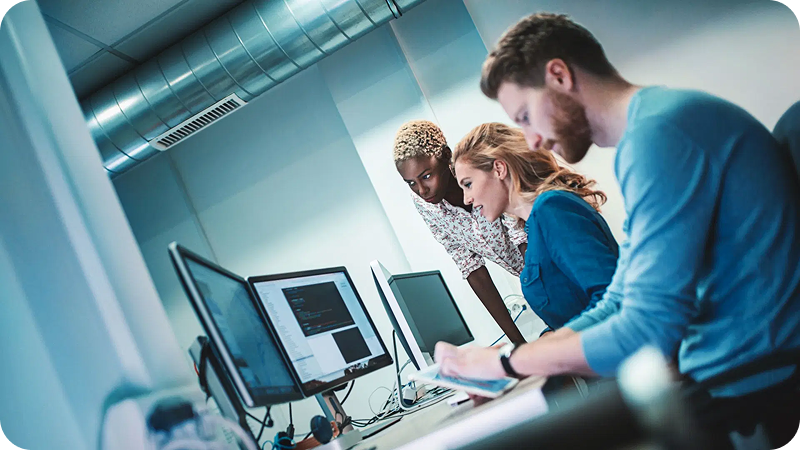 Three colleagues collaborating and working on computers in a modern office setting.